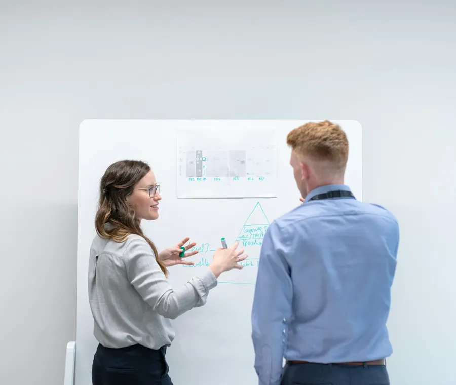 Two colleagues working through a plan on a whiteboard