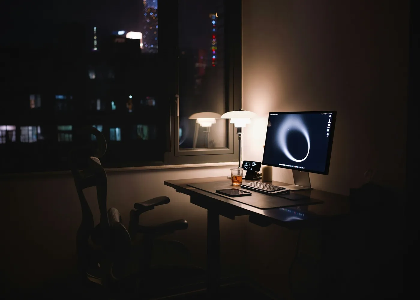 A desk with a monitor and lamp in a quiet office at night